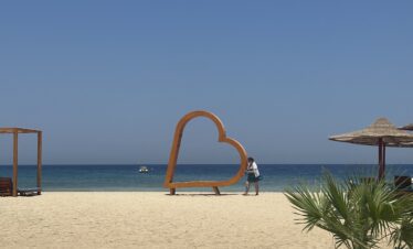 Une plage de sable fin avec une grande sculpture en forme de cœur face à la mer.