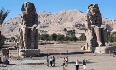 Deux statues monumentales des Colosses de Memnon à Louxor, Égypte, entourées de paysages désertiques et ciel clair.