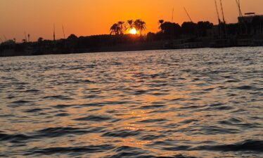 Vue sur le Nil au coucher du soleil depuis une felouque à Louxor, avec des reflets dorés sur l’eau.