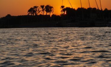 Vue sur le Nil au coucher du soleil depuis une felouque à Louxor, avec des reflets dorés sur l’eau.