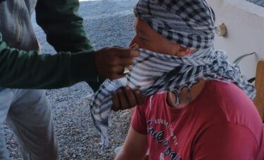 Un touriste et un guide local en train de préparer un keffiyeh avant une aventure dans le désert.
