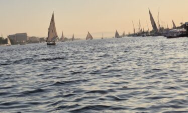 Vue sur le Nil au coucher du soleil depuis une felouque à Louxor, avec des reflets dorés sur l’eau.