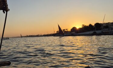 Vue sur le Nil au coucher du soleil depuis une felouque à Louxor, avec des reflets dorés sur l’eau.