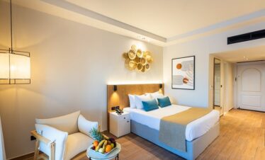 Chambre moderne et épurée avec lit double, fauteuil et petite console avec fruits frais.