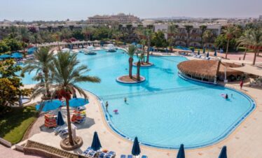 Vue aérienne spectaculaire de la grande piscine de l'hôtel entourée de palmiers et de transats.