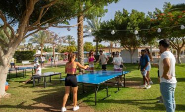 Touristes en train de jouer au tennis de table dans un cadre convivial, entourés d'arbres et de petits luminaires.