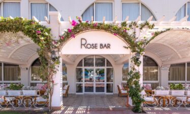 Devanture du Rose Bar, avec des voûtes décorées de roses et de plantes, des tables en bois et des coussins blancs et rouges.