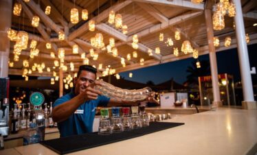 Bar extérieur de l'hôtel avec barman en action, entouré de luminaires suspendus.