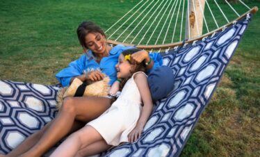 Maman et fille détendues sur un grand hamac à motifs bleu et blanc dans le jardin de l'hôtel.
