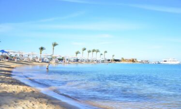 Vue sur la plage privée de l'hôtel, avec des parasols, des palmiers et du sable doré.