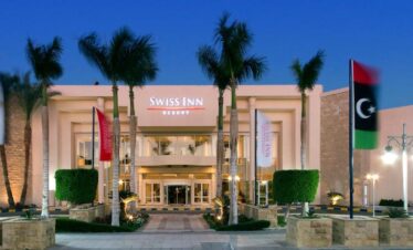 Façade de l’hôtel Swiss Inn Resort avec drapeaux, palmiers et décoration soignée.