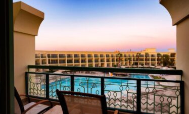 Terrasse d’une chambre avec deux fauteuils, une table et vue sur la piscine de l’hôtel.