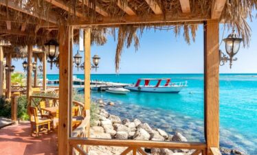 Vue depuis le restaurant en bord de plage, face à la mer, avec un ponton menant à de petits bateaux.