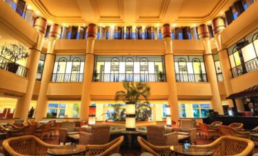 Salle de réception spacieuse avec des tables simples en marbre ou en verre et des chaises en osier, entourée de deux étages.