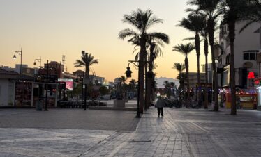 Ruelle de Hurghada bordée de palmiers et de boutiques au coucher du soleil.
