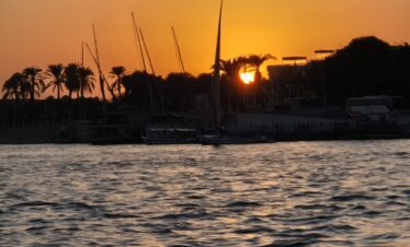 Vue sur le Nil au coucher du soleil depuis une felouque à Louxor, avec des reflets dorés sur l’eau.