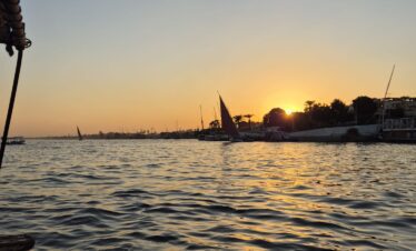 Vue sur le Nil au coucher du soleil depuis une felouque à Louxor, avec des reflets dorés sur l’eau.