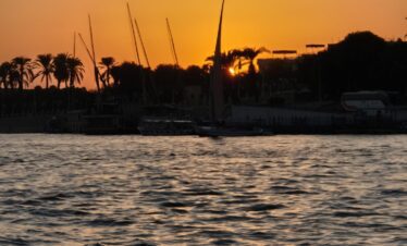 Vue sur le Nil au coucher du soleil depuis une felouque à Louxor, avec des reflets dorés sur l’eau.