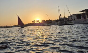 Vue sur le Nil au coucher du soleil depuis une felouque à Louxor, avec des reflets dorés sur l’eau.
