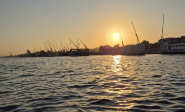 Vue sur le Nil au coucher du soleil depuis une felouque à Louxor, avec des reflets dorés sur l’eau.
