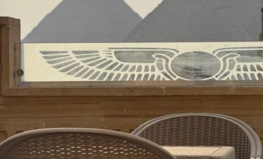 Table et chaises en osier sur un rooftop avec vue sur les pyramides.