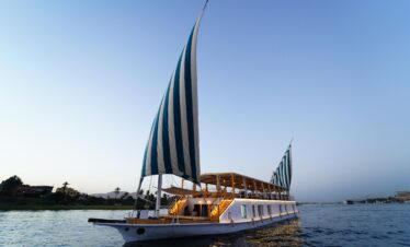 Bateau Dahabiya naviguant sur le Nil dans une ambiance magique au crépuscule, lanternes allumées illuminant le pont pour une croisière romantique en Égypte.