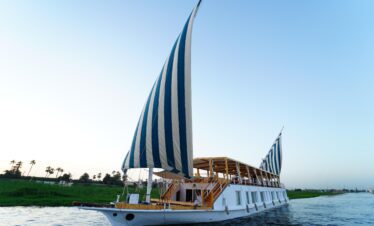 Bateau Dahabiya naviguant sur le Nil en plein jour, design traditionnel avec voiles élégantes et ambiance paisible pour une croisière unique en Égypte.