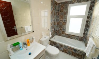 Salle de bain moderne et lumineuse à bord d’un bateau de croisière, équipée d’une baignoire ornée de mosaïques traditionnelles, d’un lavabo avec rangement, et d’accessoires soigneusement disposés pour le confort des passagers.