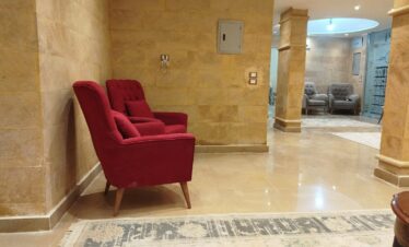 Détail du hall avec fauteuils en velours rouge et gris, tapis et piliers décoratifs.