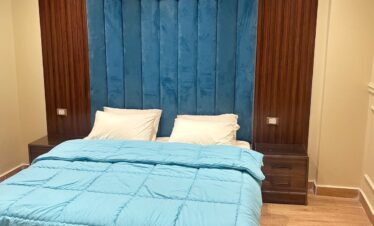 Lit en velours bleu canard avec tête de lit haute, encadré par deux murs en bois et commodes assorties.