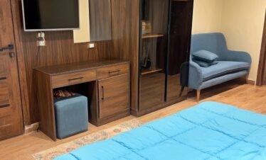 Chambre en bois avec lit en velours bleu, commode avec miroir, placard vitré et canapé deux places.