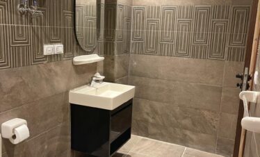 Salle d'eau moderne en carrelage gris avec fresque décorative, lavabo design et toilettes.